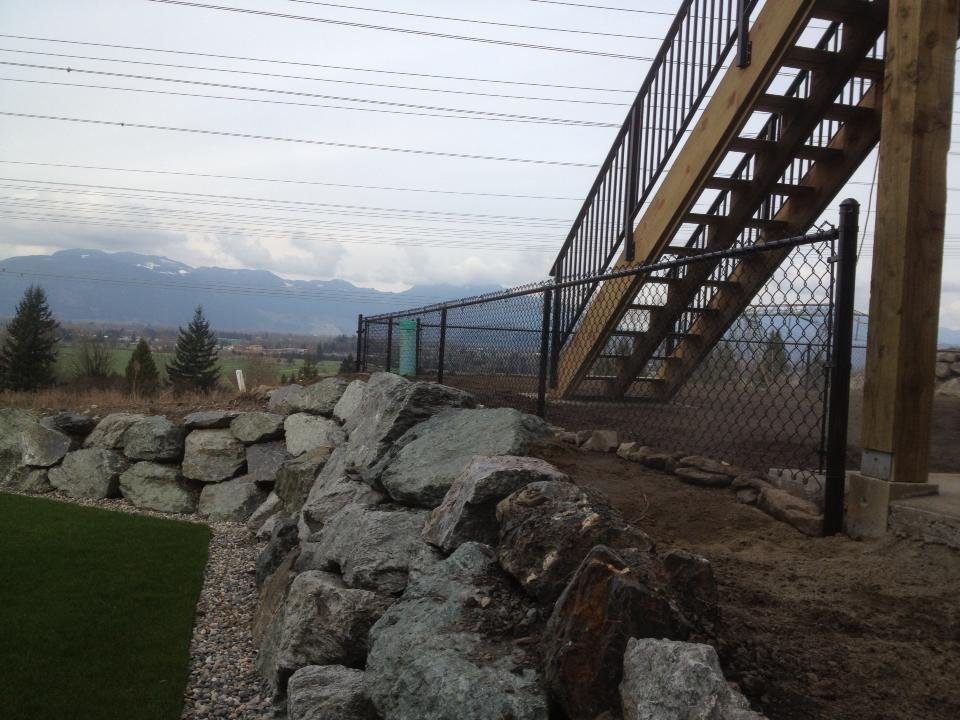 Chain link fencing installation — Chilliwack, BC Black vinyl-coated chain link fence installed along a rock-wall hillside acreage in Chilliwack BC by LS Fencing